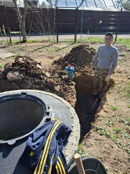 Мастер прокладывает трубу в траншее от колодца